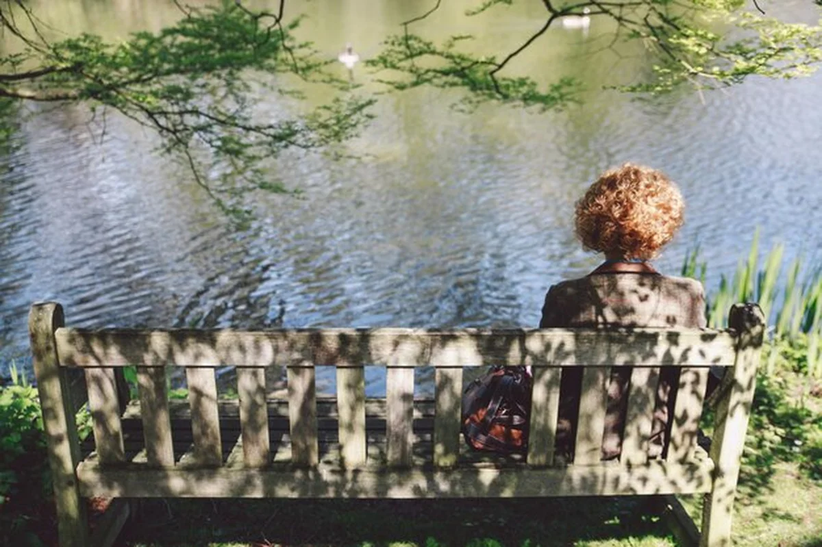 Kobieta siedząca na drewnianej ławce nad jeziorem