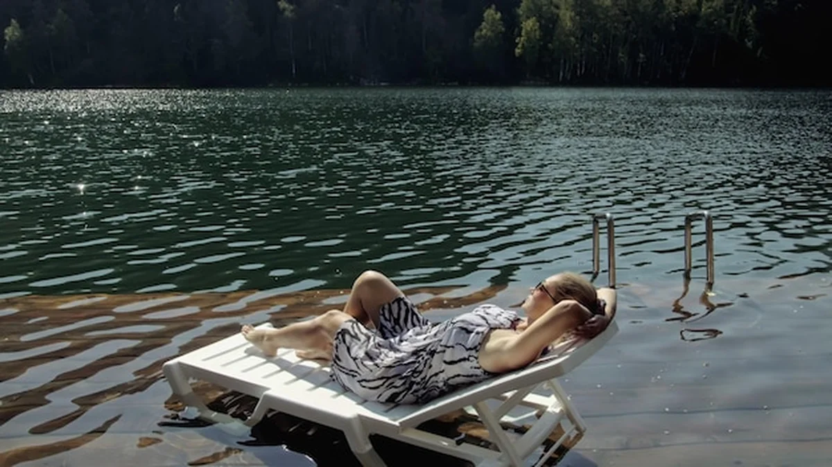Kobieta leży na leżaku w okularach przeciwsłonecznych i jedwabnym szalu obok jeziora