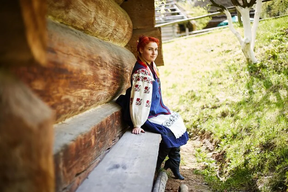 Młoda kobieta w tradycyjnym stroju ukraińskim przed drewnianym domem