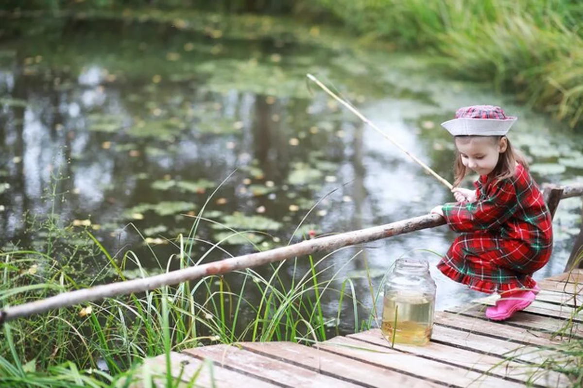 Dziecko łowi ryby nad stawem w jesienny poranek. Rybak z wędką na chodniku podczas zachodu słońca