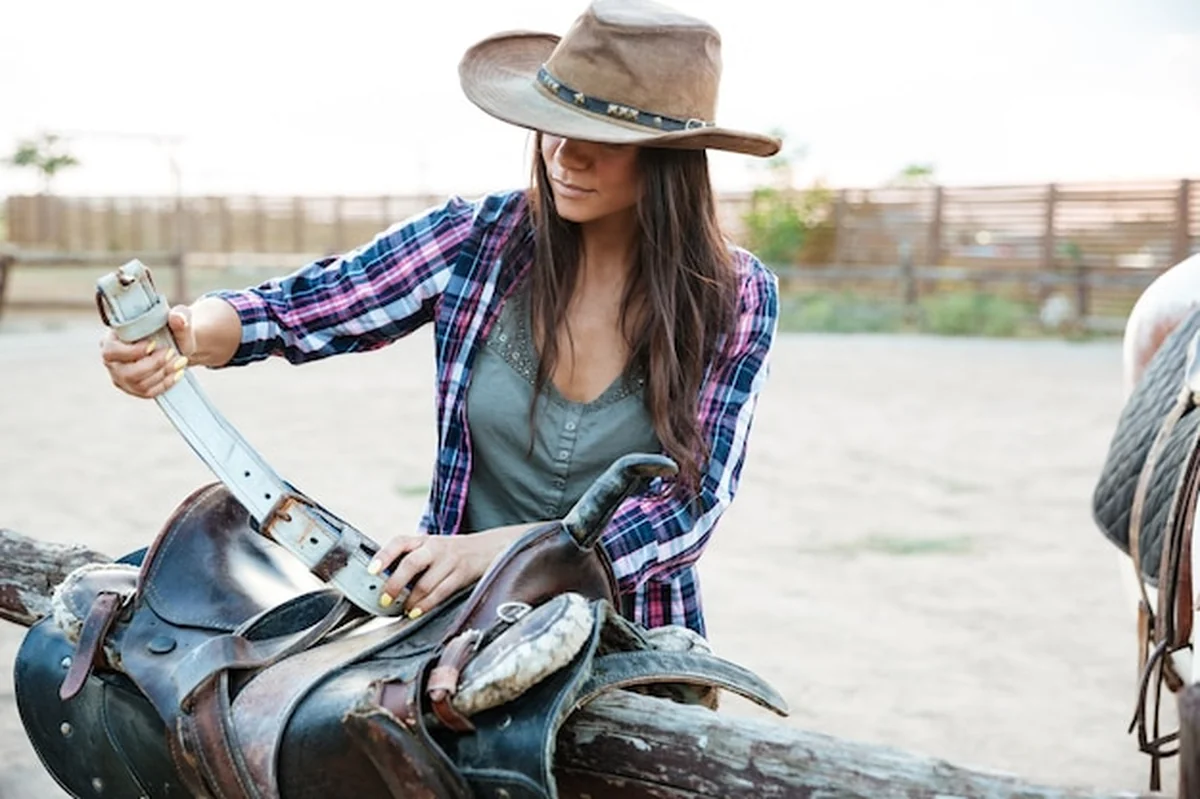 Młoda kobieta kowbojka przygotowuje siodło do jazdy konnej