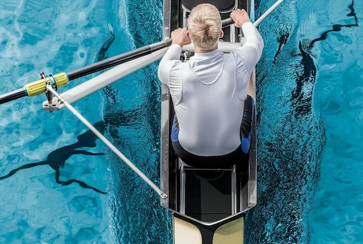 Młody mężczyzna wiosłuje łodzią na rzece