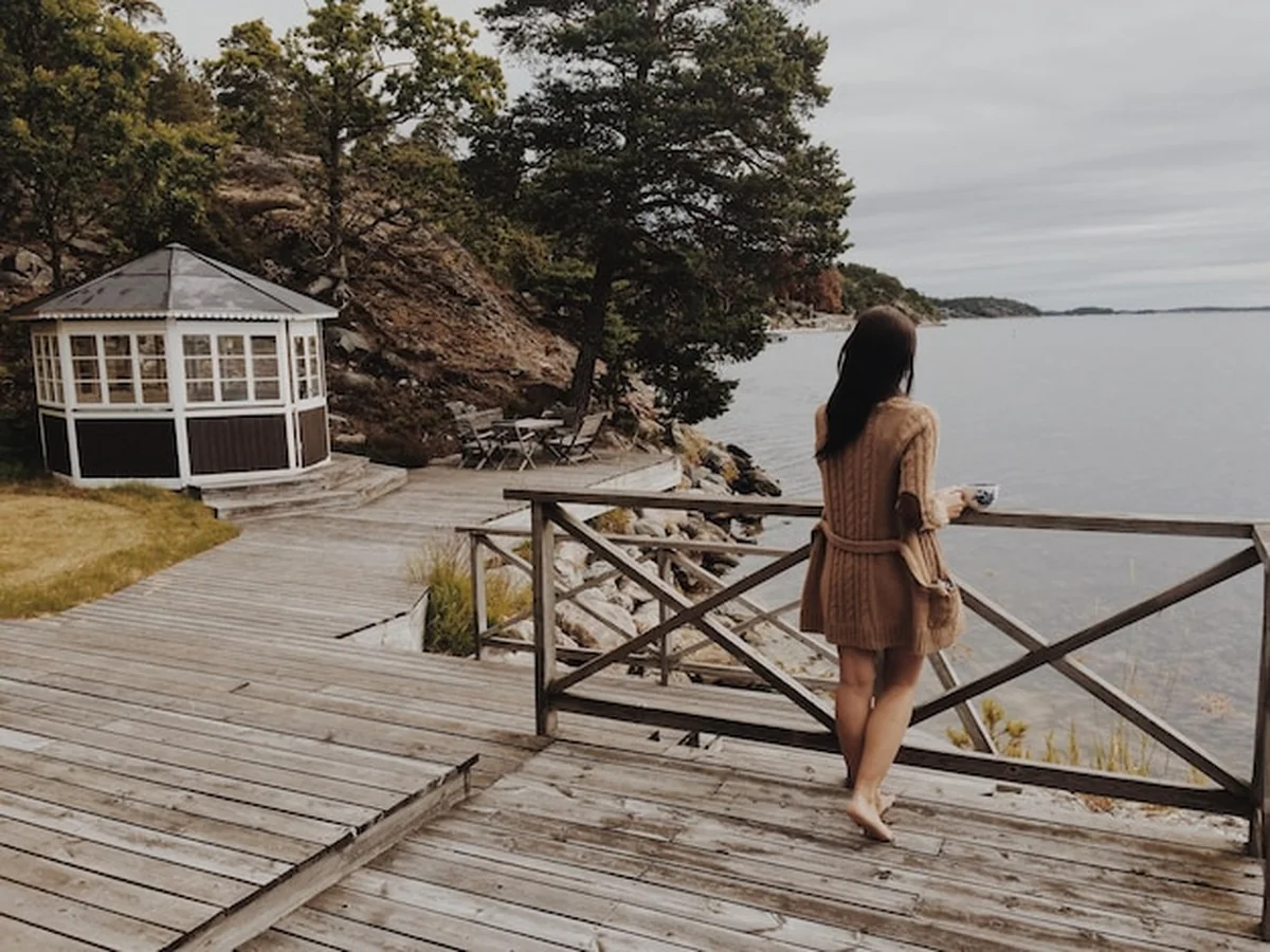 Młoda kobieta z kawą na tarasie chatki nad jeziorem w jesienny poranek