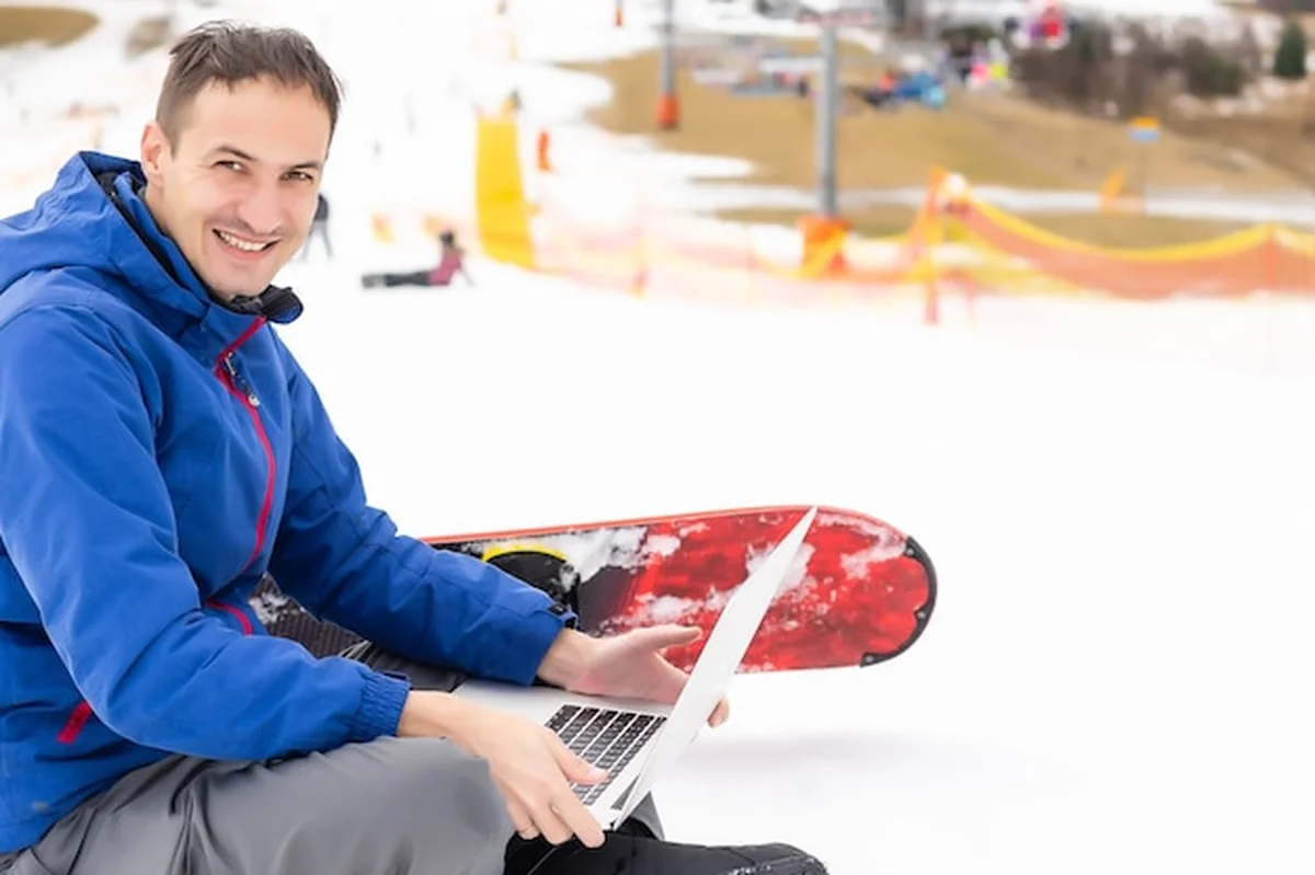 Młody snowboardzista na zaśnieżonej górze z laptopem