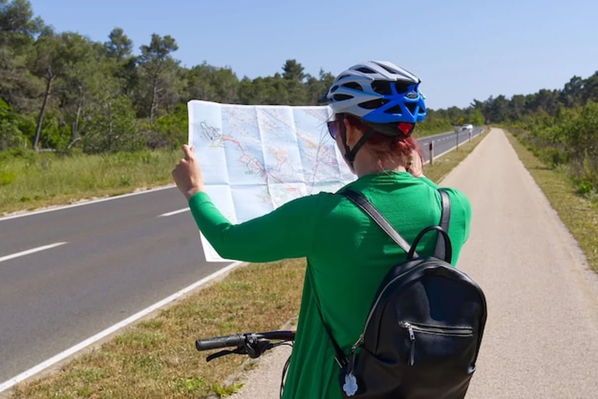 Turystyczna dziewczyna na rowerze oglądająca mapę na skrzyżowaniu dróg rowerowych