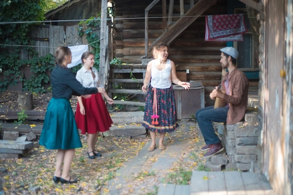 Ludzie rozmawiają z muzykiem grającym na bałałajce przed wiejskim domem