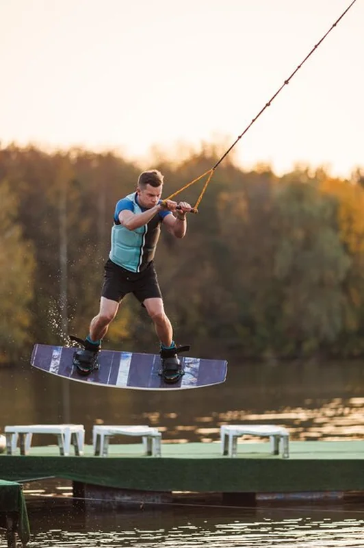 Wakeboardziści skaczą na desce wodnej przy tle lasu i zachodu słońca nad jeziorem